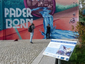 Person posiert vor einem farbenfrohen Graffiti in Paderborn, während ein Fotograf das Bild aufnimmt.