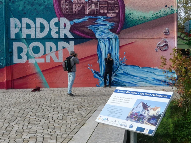 Fotoshooting vor dem Herzgarffiti Person posiert vor einem farbenfrohen Graffiti in Paderborn, während ein Fotograf das Bild aufnimmt.