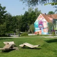 Paderborner Herzgraffiti im Mittleren Paderquellgebiet Graffiti von einem lila Monster auf einem Haus in Paderborn, umgeben von grünen Parkflächen.