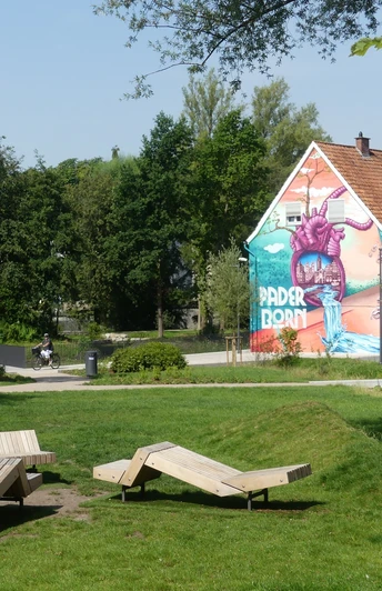 Paderborner Herzgraffiti im Mittleren Paderquellgebiet Graffiti von einem lila Monster auf einem Haus in Paderborn, umgeben von grünen Parkflächen.