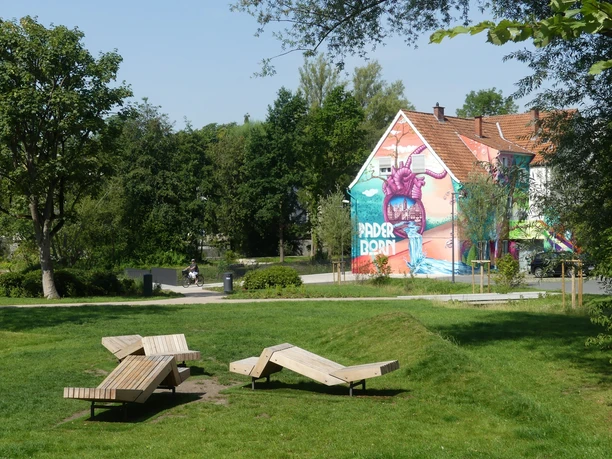 Paderborner Herzgraffiti im Mittleren Paderquellgebiet Graffiti von einem lila Monster auf einem Haus in Paderborn, umgeben von grünen Parkflächen.