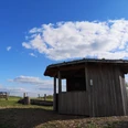 Kleine Holzschutzhütte auf einem Hügel mit weitem Blick über eine Wiesenlandschaft an einem klaren Tag.