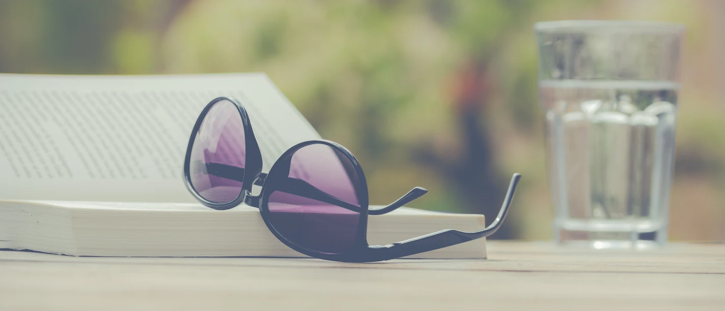 Glasses open on a book, next to a glass of water on a table.