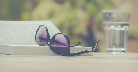 Arche-Bücherei Borkum Aufgeschlagene Brille auf einem Buch, daneben ein Glas Wasser auf einem Tisch.