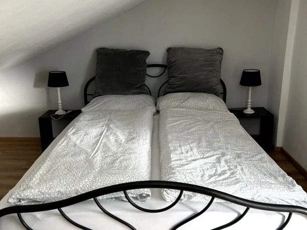 Dachgeschosszimmer mit einem eleganten, schmiedeeisernen Doppelbett zwischen zwei Nachttischen.