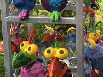 Bunte Spatzen Lieblingsort Schutzhütte Apermarsch Lebhafte, bunte Skulpturen, die Vögel darstellen, vor grünem, lebendigem Hintergrund.