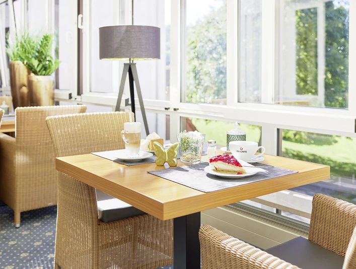 22697_Waldhotel Baerenstein_2023_Kaffee_A.jpg Heller Frühstücksraum mit geflochtenen Stühlen, Tisch mit Kaffee, Croissant und Marmelade, sonniger Ausblick.