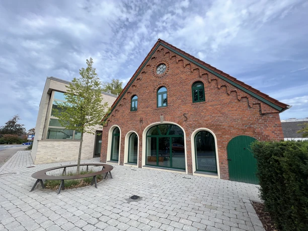 Rot verklinkertes Kulturgebäude mit gewölbten Fenstern, Ziegeldach und angrenzendem modernen Anbau.