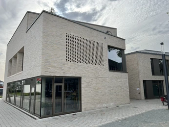 Kulturscheune Leeste VHS Modernes zweistöckiges Gebäude mit Backsteinfassade, großen Fensterfronten und einem Pflasterweg.