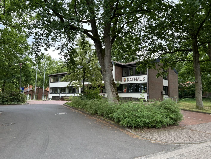 Rotes Backsteingebäude des Rathauses Kirchlinteln umgeben von grünen Bäumen und Gehwegen.