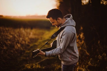 Ein Mann spielt Gitarre auf einem Feldweg bei Sonnenuntergang, umgeben von herbstlicher Natur.