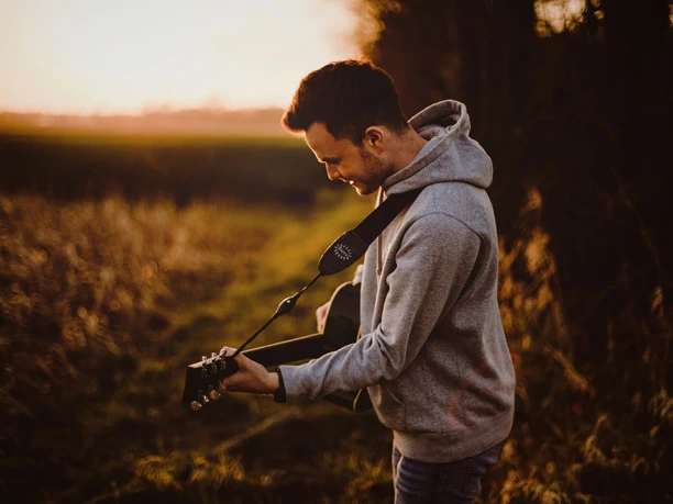Ein Mann spielt Gitarre auf einem Feldweg bei Sonnenuntergang, umgeben von herbstlicher Natur.