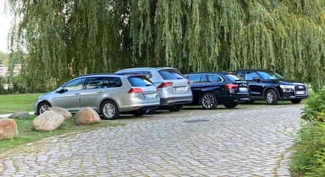 Parkplatz_Schlosswiese1_22082023_PetraRoemer.jpg Eine gepflasterte Straße führt zu den Parkmöglichkeiten. Im Hintergrund stehen Bäume