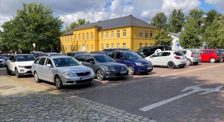 Parkplatz_Rathaus1_22082023_PetraRoemer.jpg Parkplatz mit Autos. Im Hintergrund steht das gelbe Rathaus