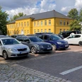 Parkplatz_Rathaus1_22082023_PetraRoemer.jpg Parkplatz mit Autos. Im Hintergrund steht das gelbe Rathaus