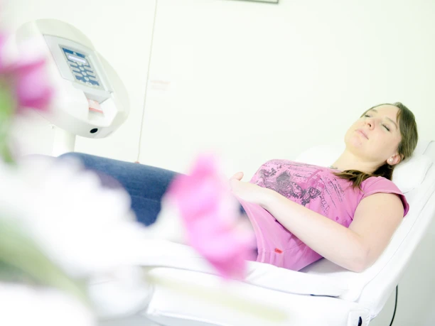 Park Klinik Wellness©Sascha Reichert-4169.jpg Eine Frau entspannt auf einer Wellness-Liege, im Vordergrund verschwommene pinke Blumen.