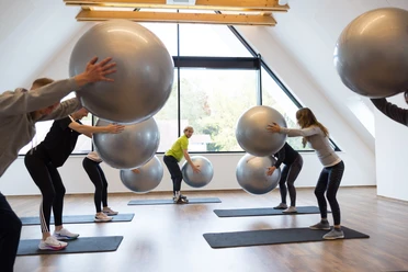 221021-FotoChristianSchwier-0790.jpg Menschen in einem Fitnessstudio trainieren mit großen Gymnastikbällen auf Matten vor einem Fenster.