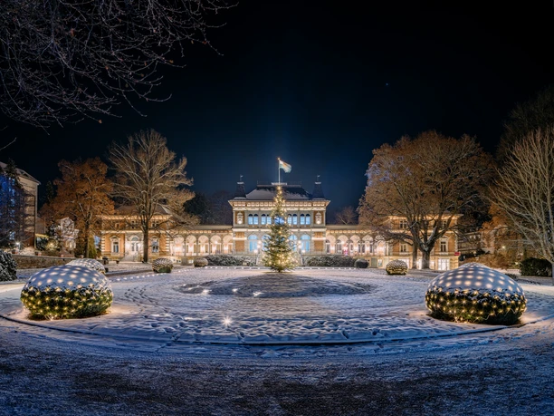 Royal spa house in winter with illuminated Christmas tree and snow-covered garden.