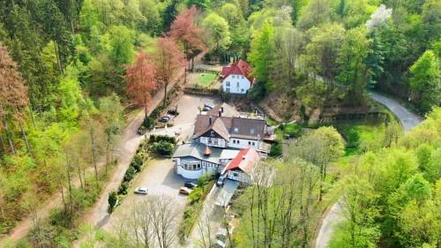 Luftaufnahme einer von Bäumen umgebenen Gebäudekomplex mit mehreren Häusern in einer grünen Landschaft.