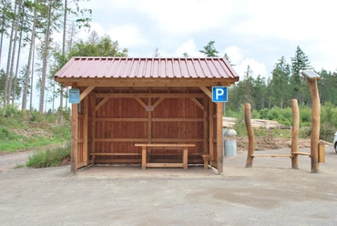 Hörstation 22 in Willebadessen Holzüberdachung mit Sitzbank im ländlichen Umfeld, Parkplatzsymbol und Informationstafeln daneben.