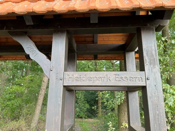 Heidepark Essern Eingangstor des Heideparks Essern aus dunklem Holz mit Jahrzahl 2001, umgeben von üppigem Grün.
