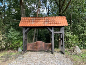 Historischer Torbogen mit roten Ziegeln und Holztor umgeben von grünem Wald im Heidepark Essern.