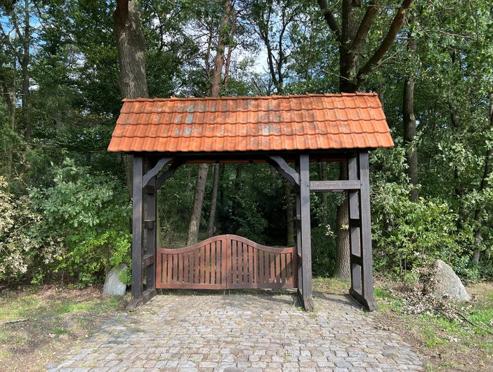 Heidepark Essern Historischer Torbogen mit roten Ziegeln und Holztor umgeben von grünem Wald im Heidepark Essern.