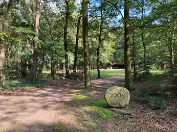 Ein gepflegter Parkweg führt zu einem großen Stein mit der Jahreszahl 2006, umgeben von Bäumen.
