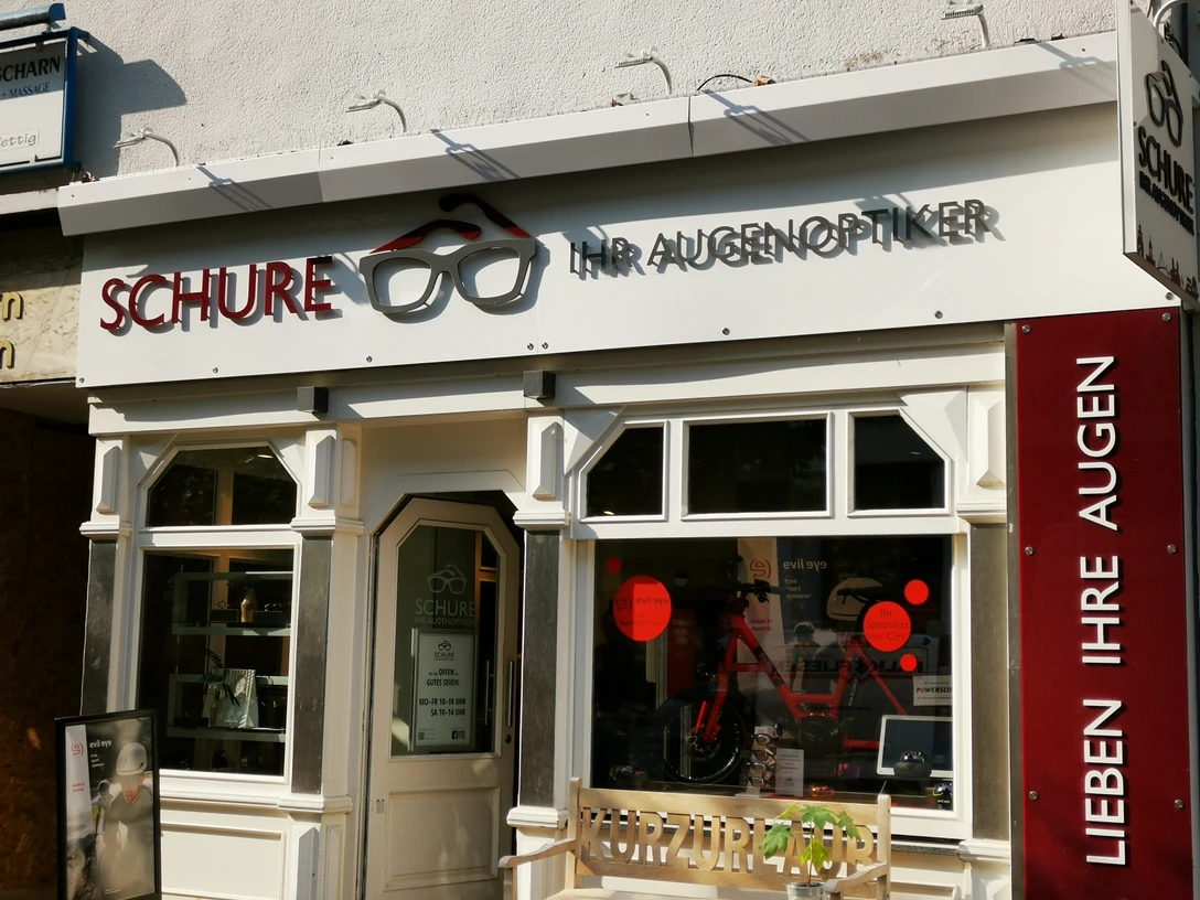Das Bild zeigt den Eingangsbereich des Geschäfts Schure. Vor dem Geschäft steht eine Bank
