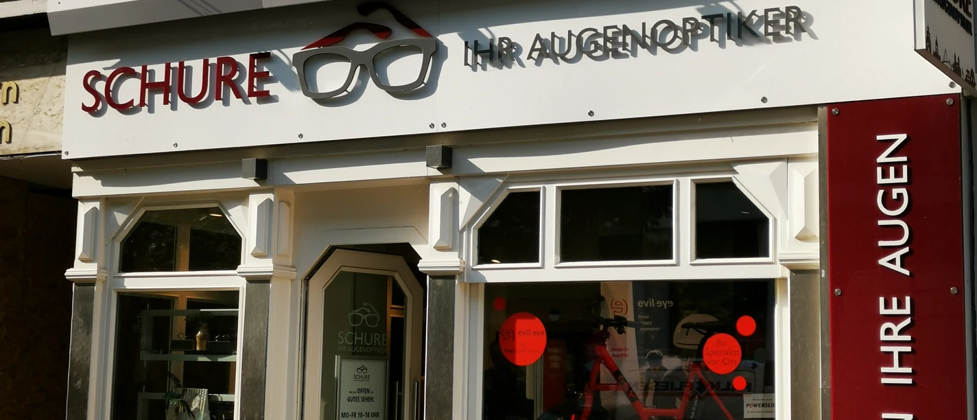 Schure.jpg Das Bild zeigt den Eingangsbereich des Geschäfts Schure. Vor dem Geschäft steht eine Bank