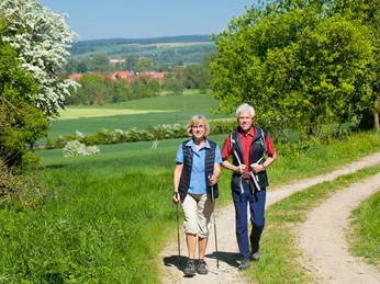 Wanderer zwischen Eberschütz und Lamerden Ein älteres Paar wandert auf einem grünen Feldweg bei sonnigem Wetter vor idyllischer Naturkulisse.
