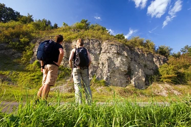 Wellenkalk am Prallhang Schwiemelkopf Zwei Wanderer betrachten eine beeindruckende Steilwand aus Wellenkalk unter einem klaren Himmel.