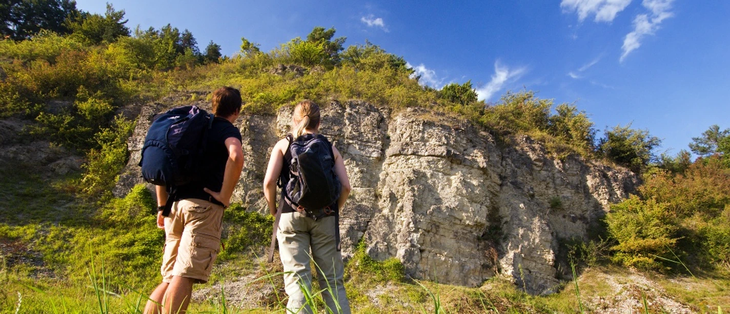 Wellenkalk am Prallhang Schwiemelkopf Zwei Wanderer betrachten eine beeindruckende Steilwand aus Wellenkalk unter einem klaren Himmel.