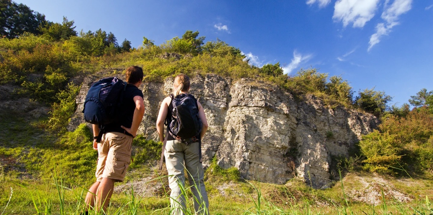 Wellenkalk am Prallhang Schwiemelkopf Zwei Wanderer betrachten eine beeindruckende Steilwand aus Wellenkalk unter einem klaren Himmel.
