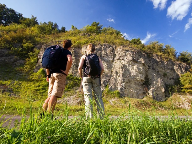 Wellenkalk am Prallhang Schwiemelkopf Zwei Wanderer betrachten eine beeindruckende Steilwand aus Wellenkalk unter einem klaren Himmel.