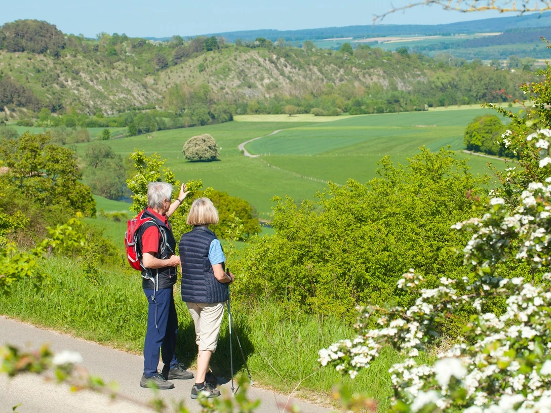 Wanderer bei Lamerden blicken auf Bunten Berg Eberschütz Zwei Wanderer betrachten eine weitläufige Landschaft mit grünen Feldern und bewaldeten Hügeln.
