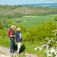 Wanderer bei Lamerden blicken auf Bunten Berg Eberschütz Zwei Wanderer betrachten eine weitläufige Landschaft mit grünen Feldern und bewaldeten Hügeln.