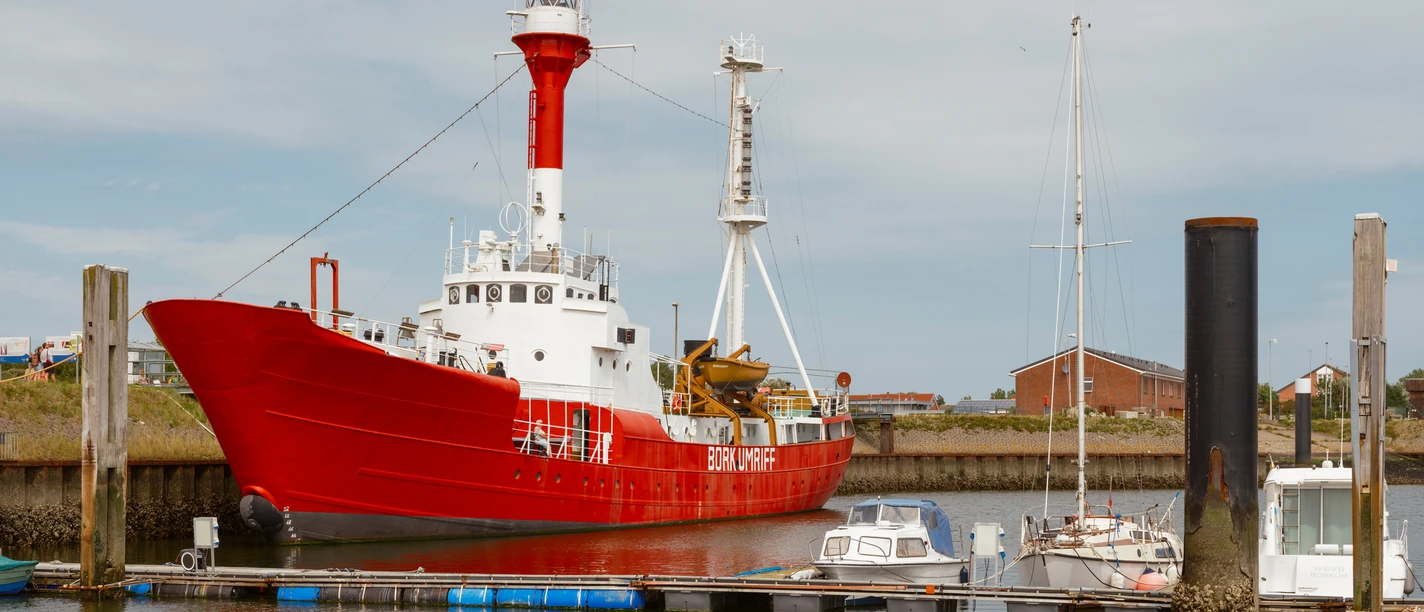 Nationalpark-Schiff Feuerschiff Borkumriff (2).jpg Das rot-weiße Feuerschiff liegt im Borkumer Hafen. Der Himmel ist grau bewölkt.