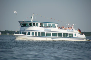fahrgastschiff-steinhude-personenschifffahrt Weißes Passagierschiff der Steinhuder Personenschifffahrt auf dem Wasser, mit Menschen an Bord.