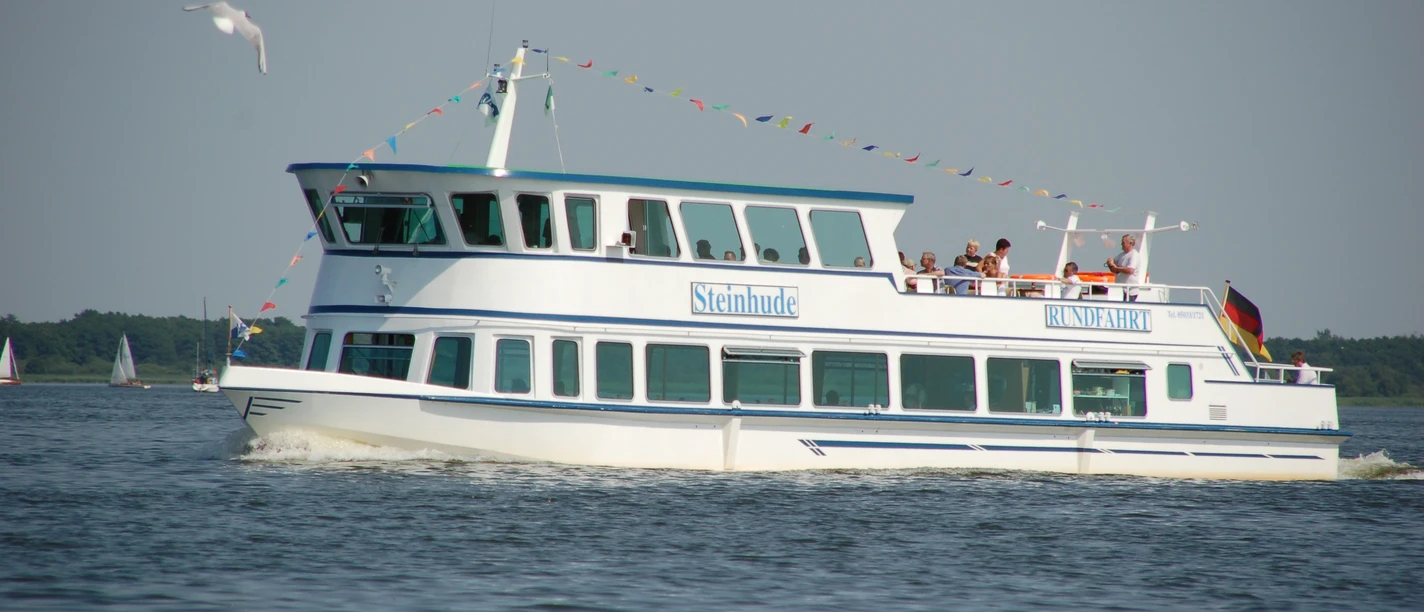 fahrgastschiff-steinhude-personenschifffahrt Weißes Passagierschiff der Steinhuder Personenschifffahrt auf dem Wasser, mit Menschen an Bord.