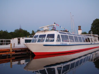 FGS Steinhude am Steg Großes Ausflugsschiff mit bunten Flaggen, angelegt an einem Steg, spiegelnd im ruhigen Wasser.Large excursion boat with colorful flags, moored at a jetty, reflecting in the calm water.En stor udflugtsbåd med farverige flag ligger fortøjet ved en anløbsbro og spejler sig i det rolige vand.Grote excursieboot met kleurrijke vlaggen, aangemeerd aan een steiger, weerspiegeld in het kalme water.