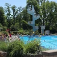 Ein Freibad mit Sprungturm, umgeben von Bäumen und bunten Blumen am Beckenrand.