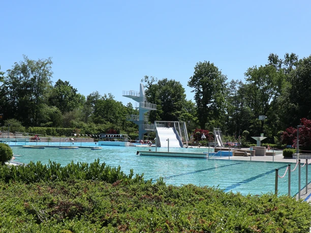 Freibad mit mehreren Pools, Rutschen und Sprungturm, umgeben von grüner Vegetation und Bäumen.