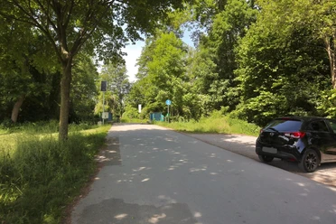 Parkplatz Leinenweg Straße am Waldrand mit geparktem schwarzem Auto, umgeben von üppigem grünem Laub und Bäumen.