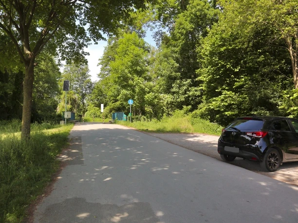 Parkplatz Leinenweg Straße am Waldrand mit geparktem schwarzem Auto, umgeben von üppigem grünem Laub und Bäumen.