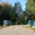 Ein geteilter Rad- und Fußweg führt über eine Brücke, gesäumt von Bäumen, mit Schranken am Eingang.