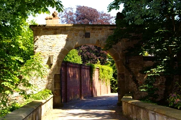 Gut Hange ( Fazenda da Esperanca ) Steinernes Tor mit Löwenskulptur führt durch eine alte Mauer, umgeben von Bäumen und Sonnenlicht.