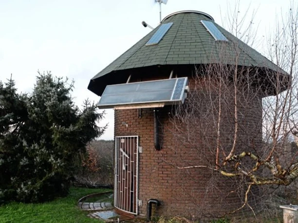 sternwarte-2 Rundes Backsteingebäude mit grünem Dach und Solarpanelen, umgeben von Bäumen und Sträuchern.