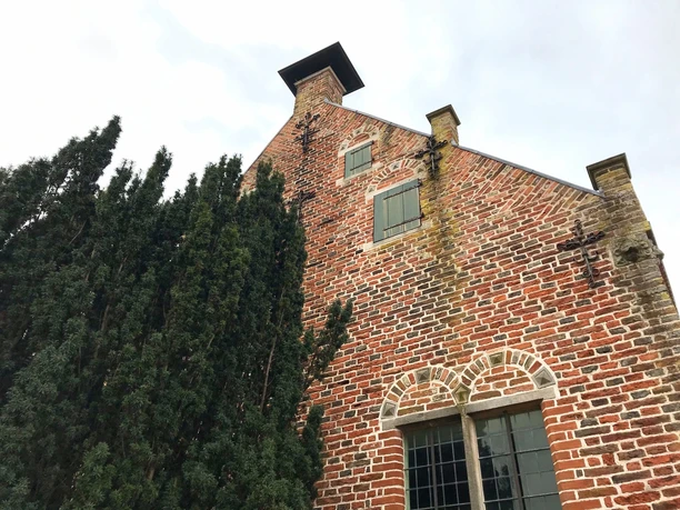 Steinhaus Greetsiel Rote Backsteinfassade des historischen Steinhauses in Greetsiel mit verzierten Giebeln und Bäumen.