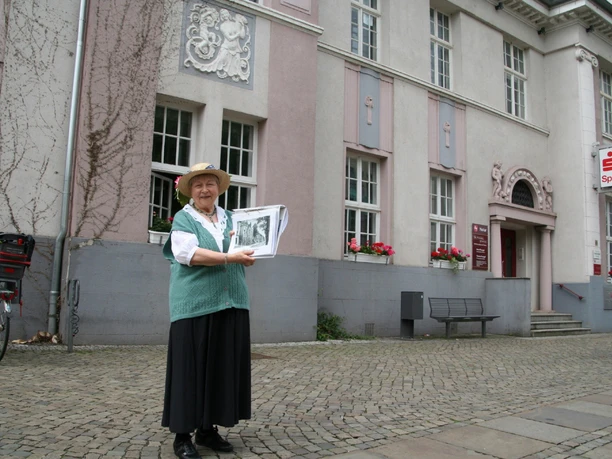 "Bürgerin Gesine" vor der Sparkasse Achim Gesine, eine ältere Frau in traditioneller Kleidung, steht lächelnd vor der Sparkasse Achim.